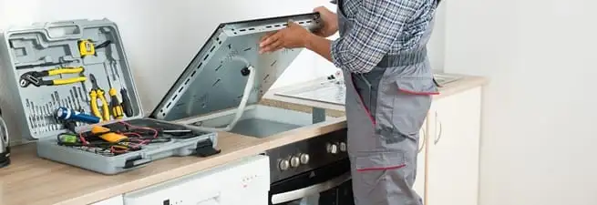 Cooktop repair technician lifting a built-in stovetop for service in Memphis, TN