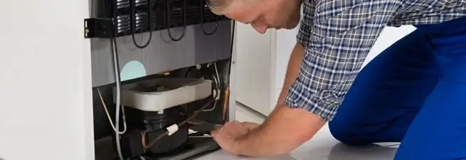 Refrigerator repair technician servicing the compressor and condenser area in Memphis, TN