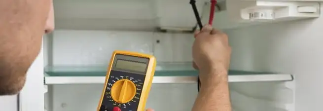 Refrigerator repair technician testing electrical components with a multimeter in Memphis, TN
